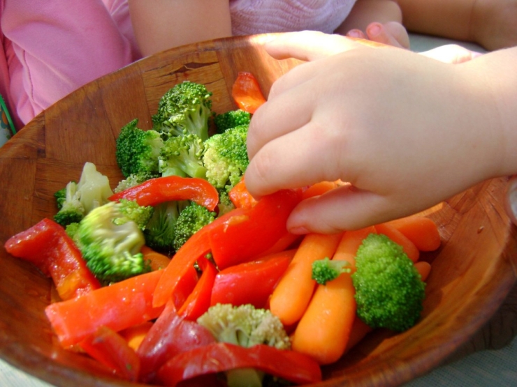 child taking red pepper from vegetable bowl